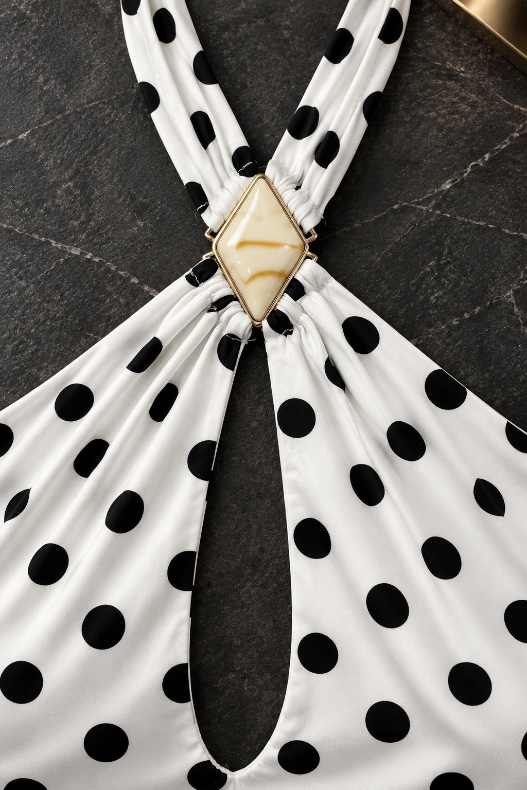 Détail du bijou doré au centre du décolleté de la robe à pois