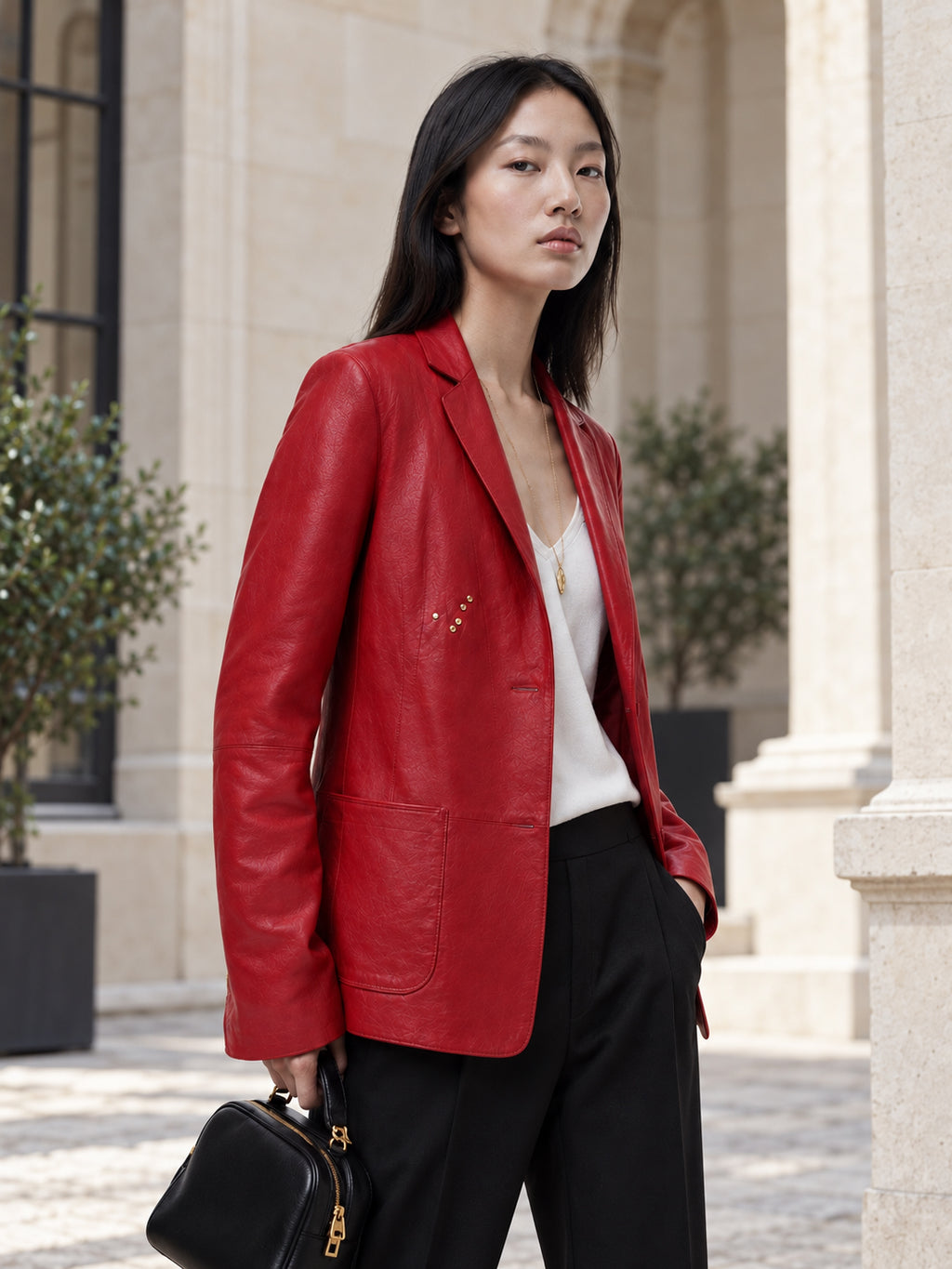 Femme portant la veste blazer rouge en cuir d'agneau DIFFERENT avec pantalon noir et sac à main, devant des colonnes en pierre – DIFFERENT Paris