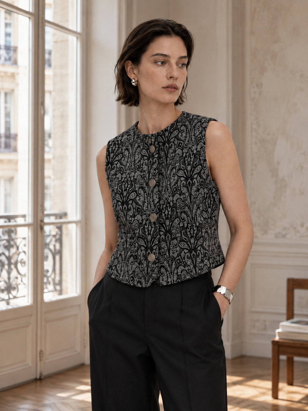 Femme portant le gilet court à motif baroque noir et gris DIFFERENT avec pantalon noir, dans un appartement haussmannien – DIFFERENT Paris