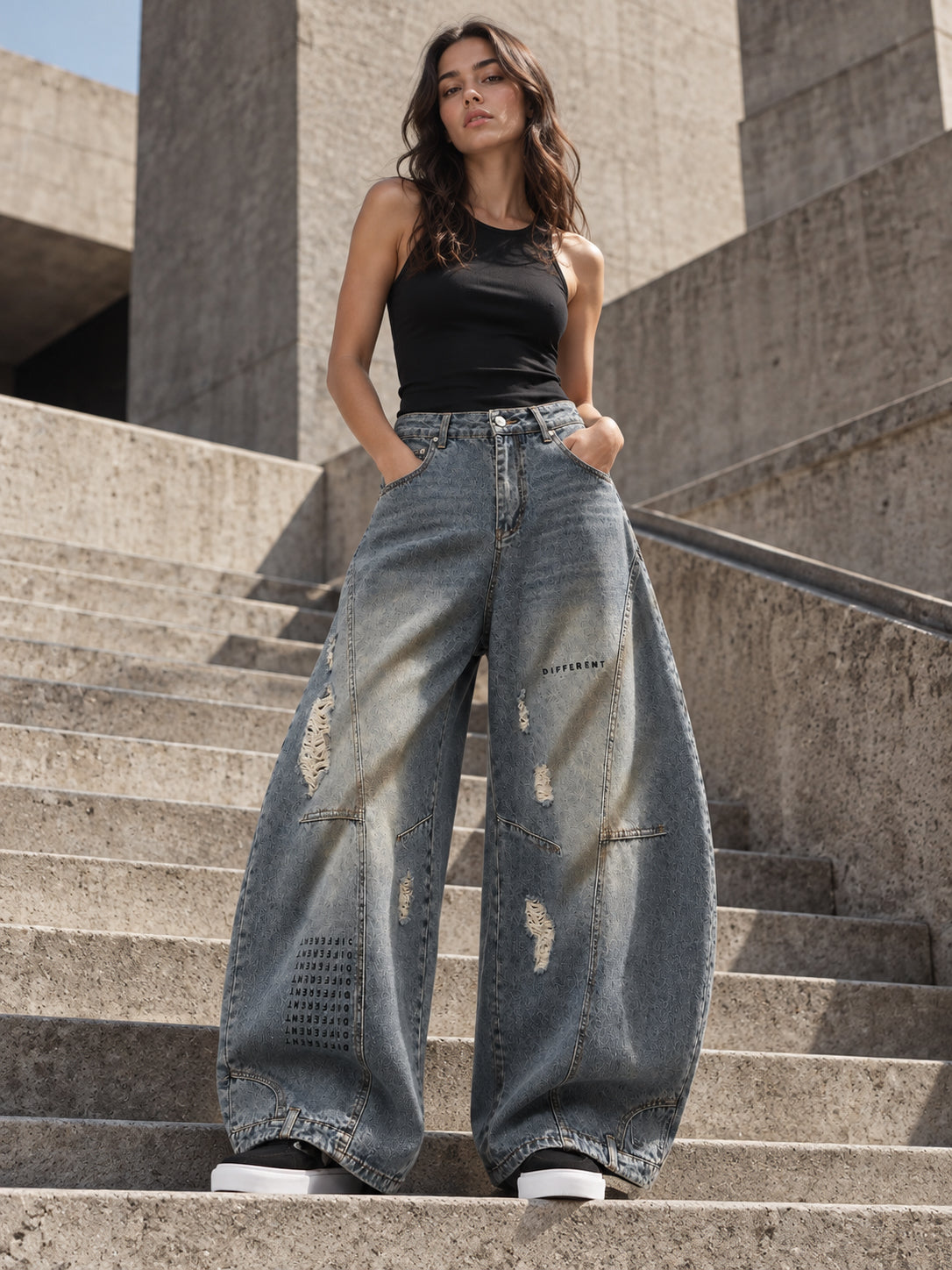 Femme portant le pantalon jean délavé oversize balloon DIFFERENT avec débardeur noir, dans un escalier en béton – DIFFERENT Paris