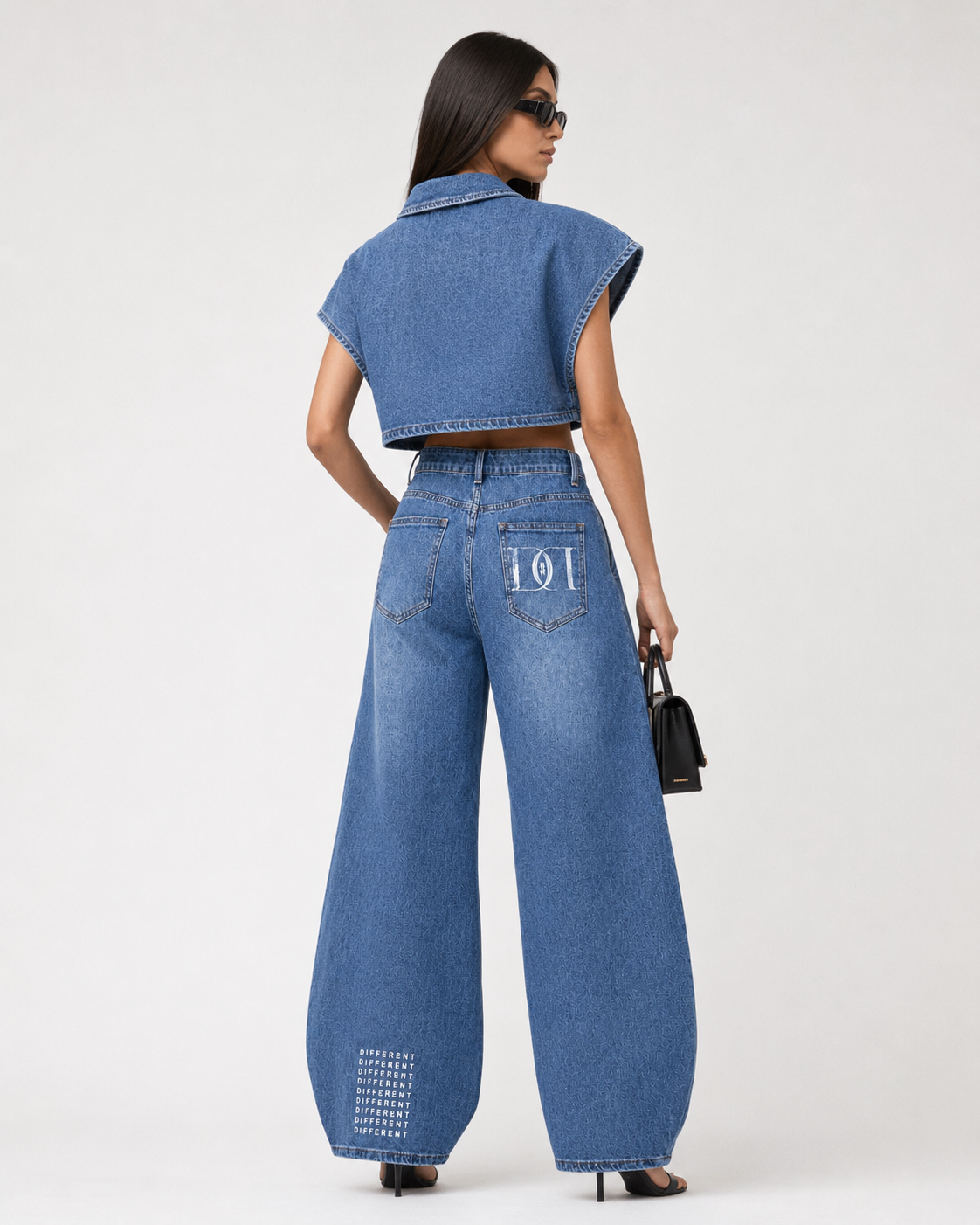 Vue de dos d’un ensemble denim femme DIFFÉRENT avec veste courte oversize, jean ballon taille haute, poches arrière graphiques et logo signature sur le bas de jambe.