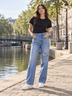 Femme portant le jean droit déchiré bleu clair DIFFERENT avec t-shirt noir, au bord d'un canal à Paris – DIFFERENT Paris