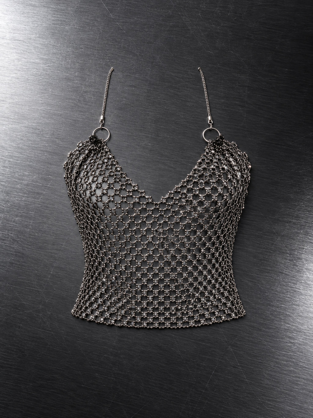 Crop top en maille diamant argentée à fines bretelles et décolleté en V, à plat sur fond gris – DIFFERENT Paris