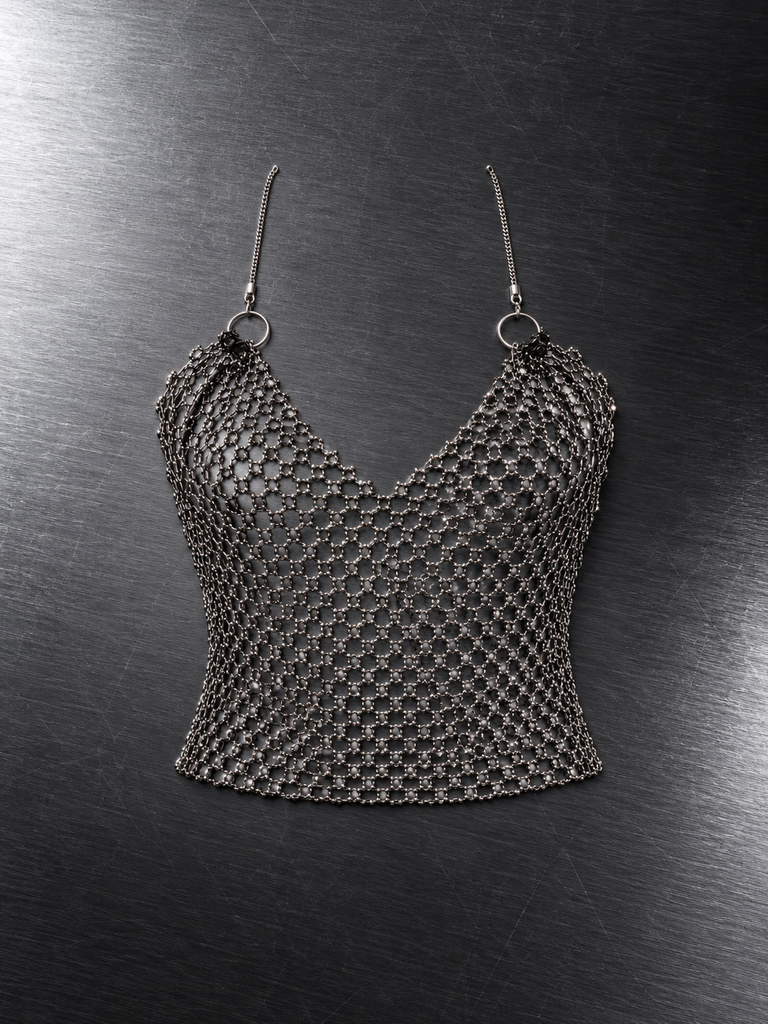Crop top en maille diamant argentée à fines bretelles et décolleté en V, à plat sur fond gris – DIFFERENT Paris