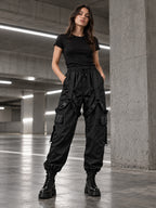 Femme portant le pantalon cargo noir à sangles DIFFERENT avec t-shirt noir et boots, dans un parking – DIFFERENT Paris