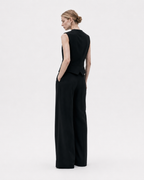 Gilet noir sans manches porté de dos avec pantalon noir large, coupe structurée et dos uni sur fond blanc.