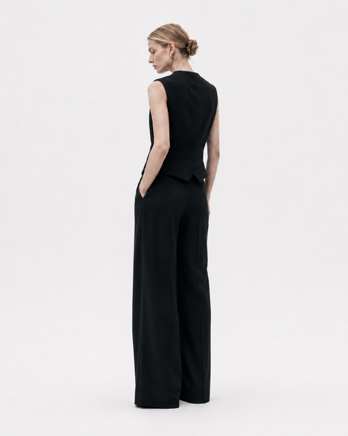 Gilet noir sans manches porté de dos avec pantalon noir large, coupe structurée et dos uni sur fond blanc.