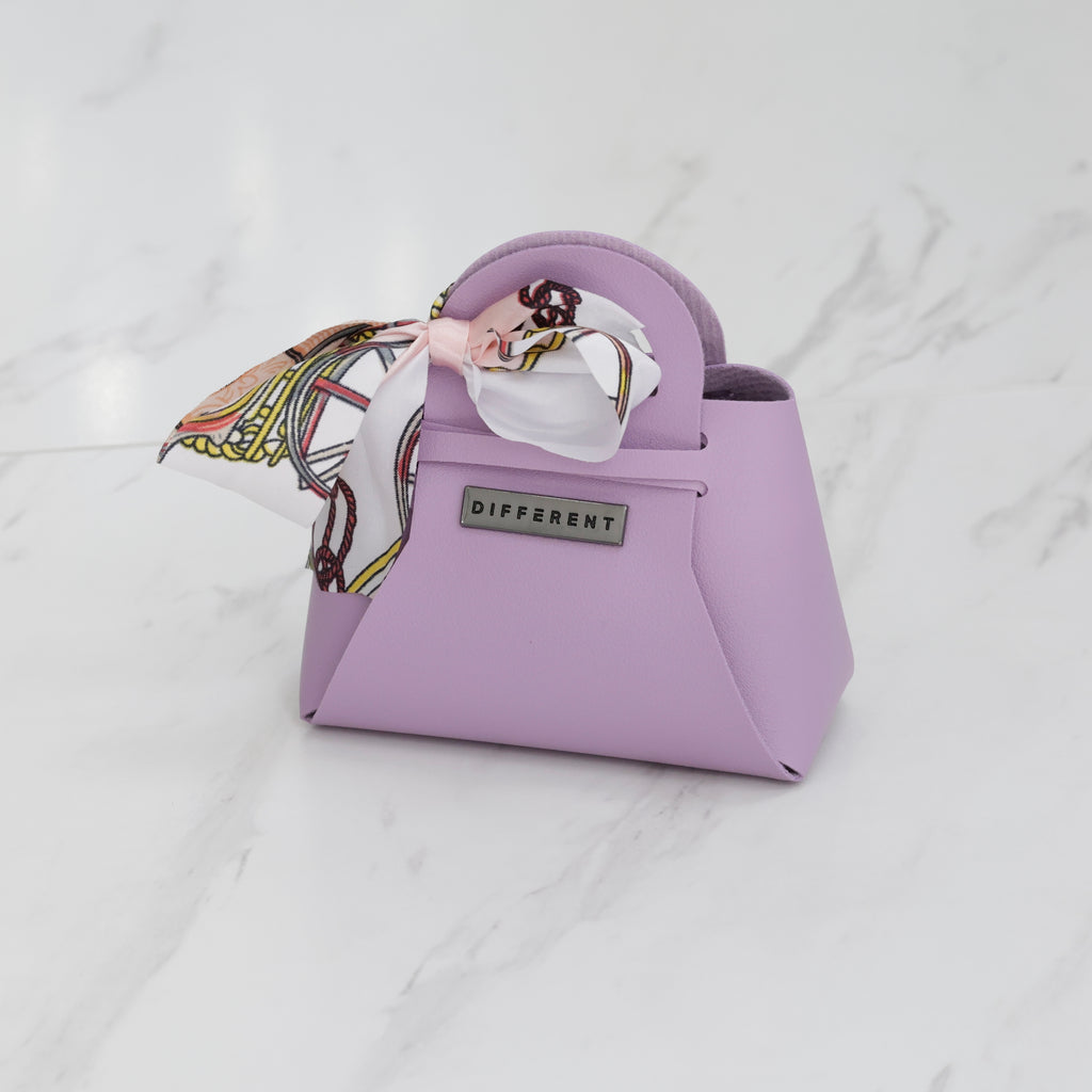 Mini sac DIFFERENT lilas avec foulard imprimé pastel, poignée arrondie et plaque logo métallique.
