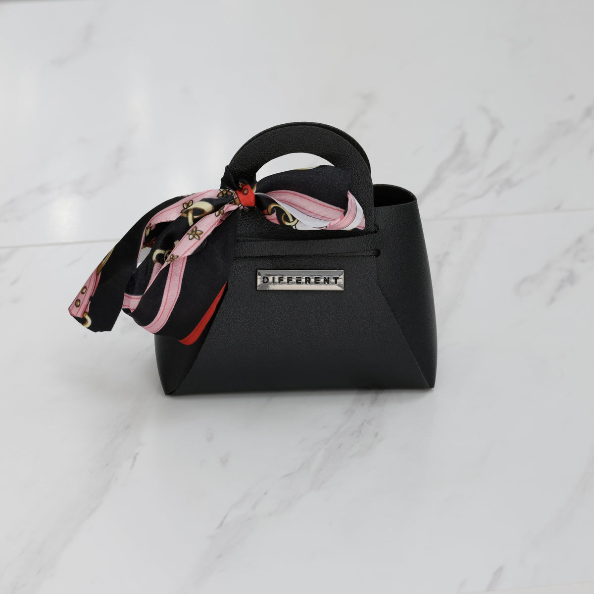 Mini sac DIFFERENT noir avec foulard imprimé rose, noir et rouge, plaque métallique siglée à l’avant.