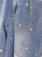 Gros plan sur denim bleu DIFFERENT avec texture délavée, surpiqûres contrastées et petits rivets métalliques décoratifs.