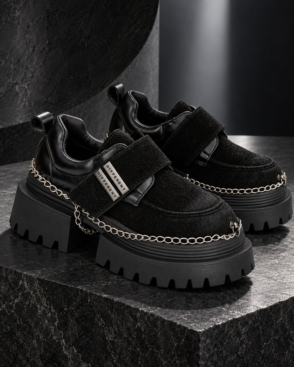 Paire de chaussures à plateforme femme noires DIFFERENT avec chaînes argentées, posée sur un socle en pierre noire – DIFFERENT Paris