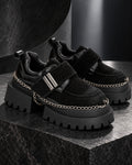 Paire de chaussures à plateforme femme noires DIFFERENT avec chaînes argentées, posée sur un socle en pierre noire – DIFFERENT Paris