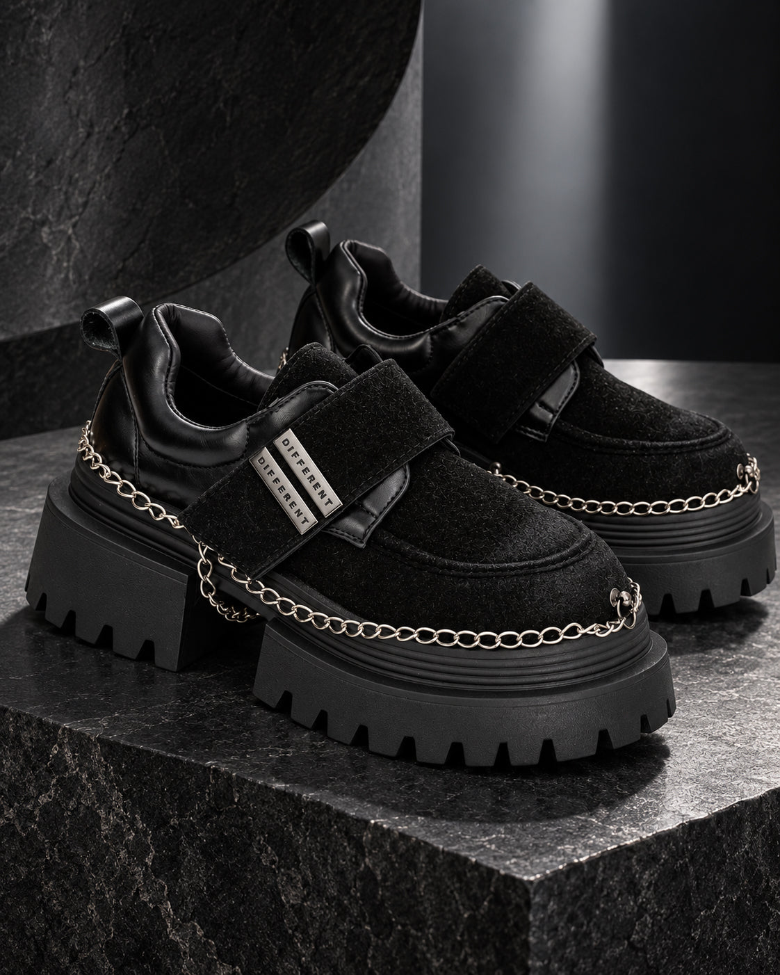 Paire de chaussures à plateforme femme noires DIFFERENT avec chaînes argentées, posée sur un socle en pierre noire – DIFFERENT Paris