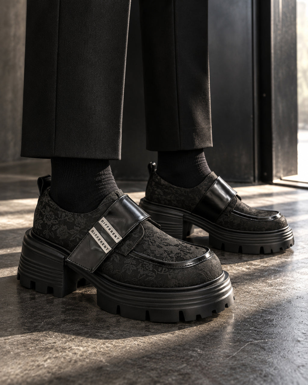 Chaussures à plateforme noir motif floral DIFFERENT portées avec pantalon noir et chaussettes noires, au seuil d'une porte – DIFFERENT Paris