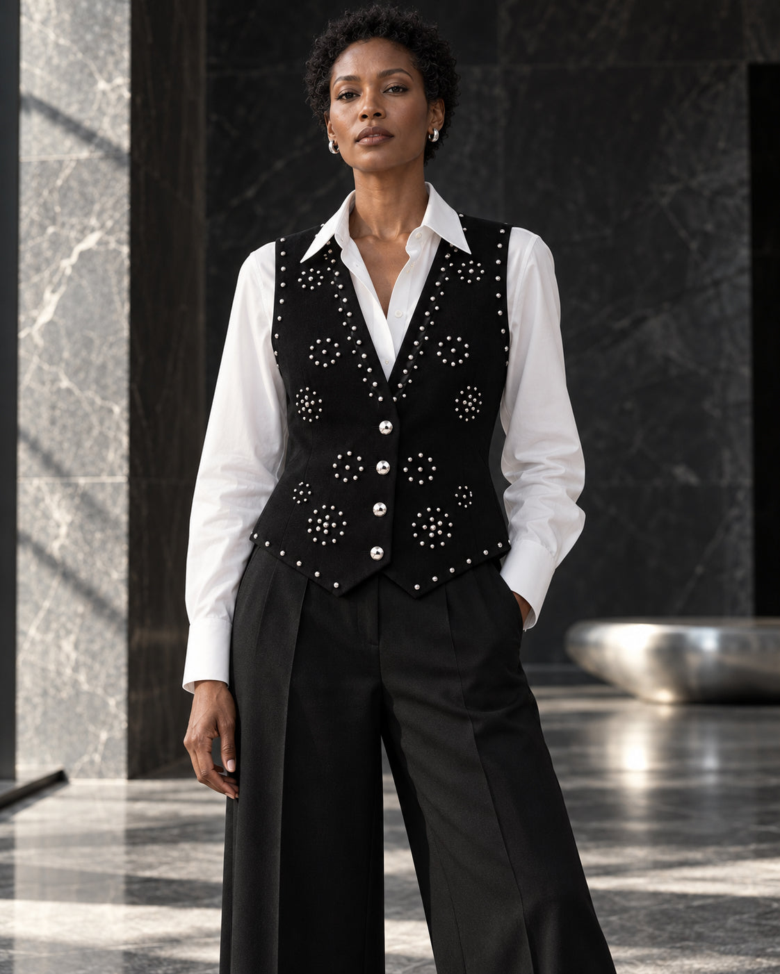 Femme portant le gilet noir structuré à clous argentés et diamants DIFFERENT avec chemise blanche et pantalon noir large – DIFFERENT Paris