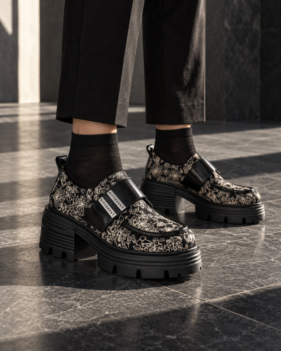 Chaussures à plateforme motif baroque DIFFERENT portées avec pantalon noir et chaussettes noires, sur dallage sombre – DIFFERENT Paris