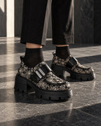 Chaussures à plateforme motif baroque DIFFERENT portées avec pantalon noir et chaussettes noires, sur dallage sombre – DIFFERENT Paris