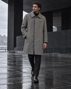 Homme portant le manteau long gris à chaînes dorées DIFFERENT, marchant sur une esplanade mouillée – DIFFERENT Paris
