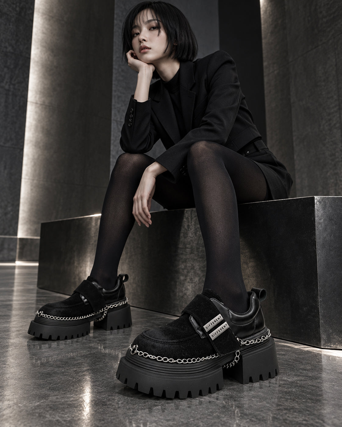 Femme assise en tailleur noir et collants noirs portant les chaussures à plateforme et chaînes DIFFERENT – DIFFERENT Paris