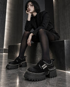 Femme assise en tailleur noir et collants noirs portant les chaussures à plateforme et chaînes DIFFERENT – DIFFERENT Paris