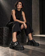 Femme assise en combinaison noire portant les chaussures à plateforme noir motif floral DIFFERENT – DIFFERENT Paris
