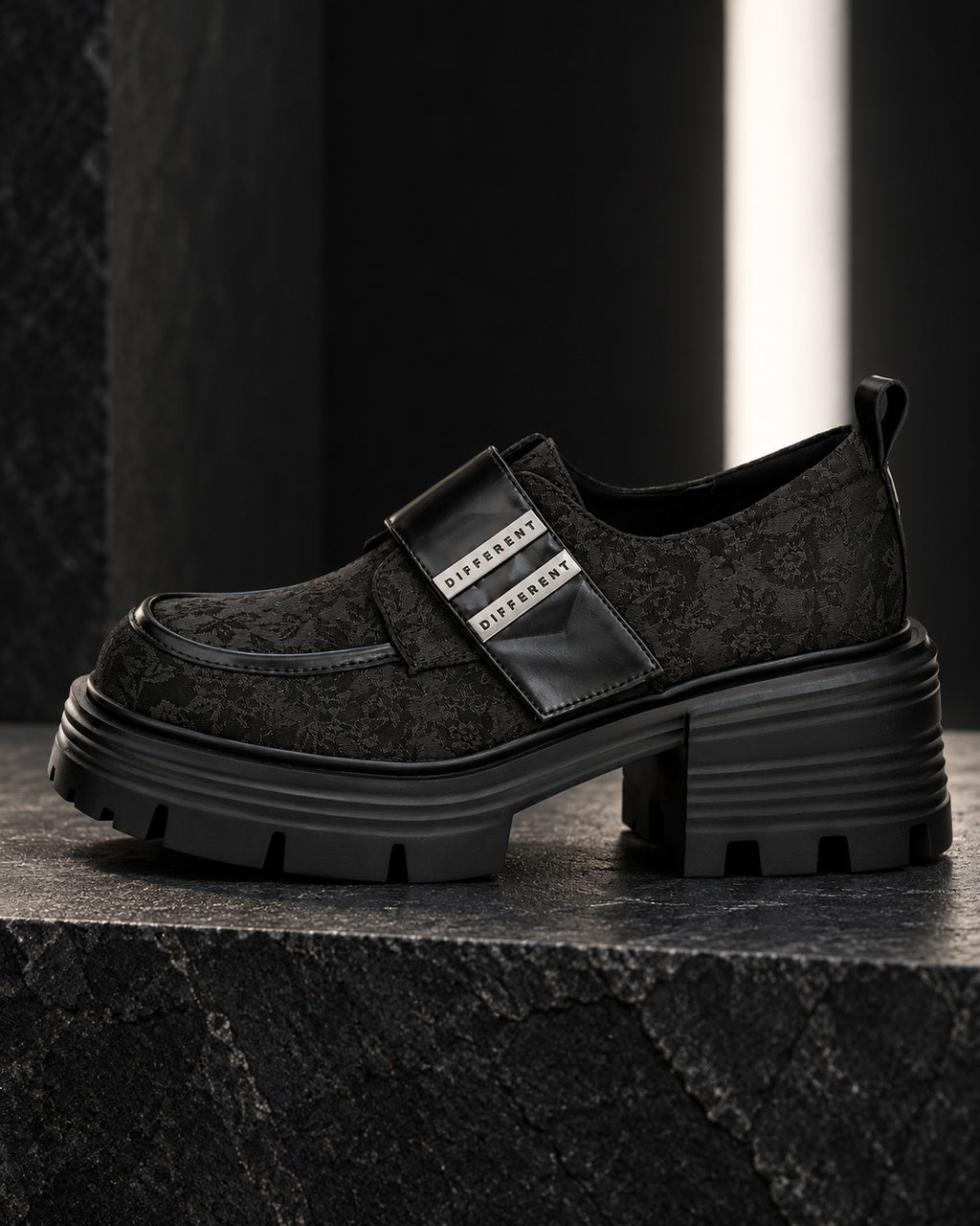 Chaussure femme à plateforme noire DIFFERENT au motif floral ton sur ton vue de profil, à contre-jour sur socle en pierre – DIFFERENT Paris