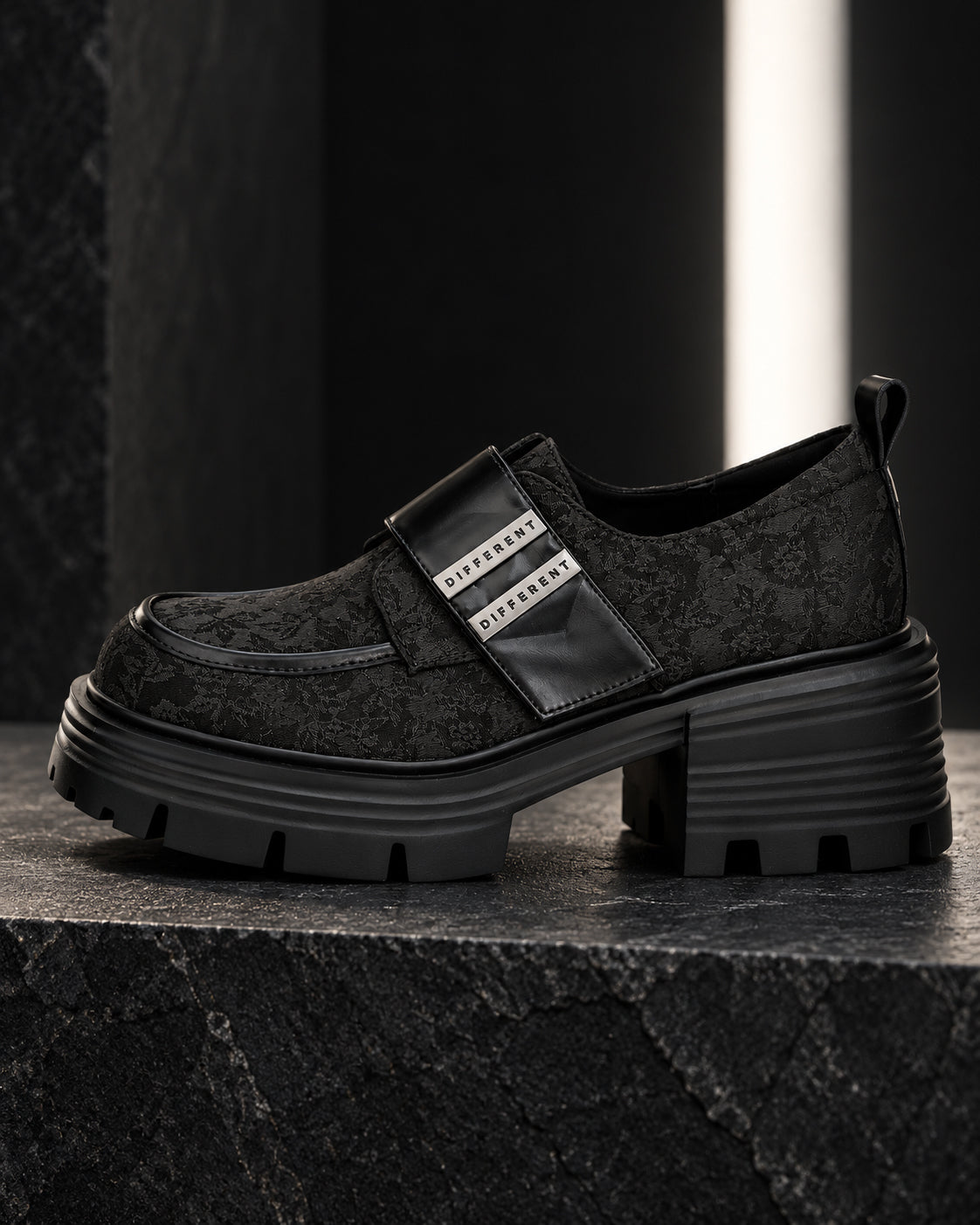 Chaussure femme à plateforme noire DIFFERENT au motif floral ton sur ton vue de profil, à contre-jour sur socle en pierre – DIFFERENT Paris
