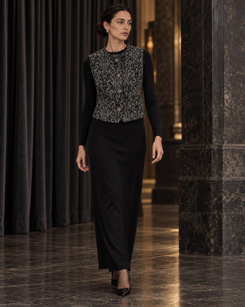 Femme portant le gilet court à motif baroque noir et gris DIFFERENT avec haut noir et jupe longue noire, dans un couloir – DIFFERENT Paris