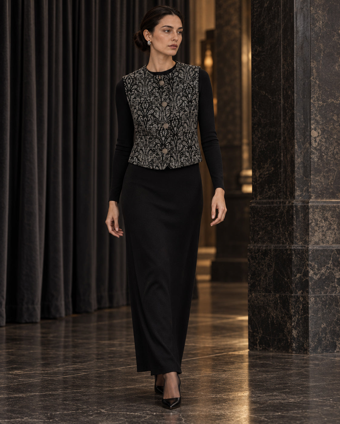 Femme portant le gilet court à motif baroque noir et gris DIFFERENT avec haut noir et jupe longue noire, dans un couloir – DIFFERENT Paris