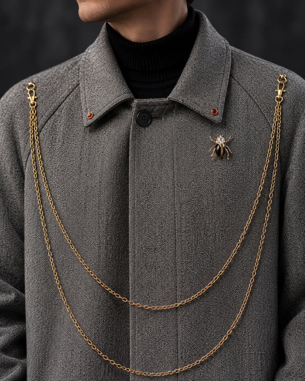 Gros plan sur le col du manteau long gris avec chaînes dorées en double rang et broche bijou – DIFFERENT Paris