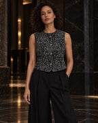 Femme portant le gilet court sans manches à motif baroque noir et gris DIFFERENT avec pantalon noir, dans un salon – DIFFERENT Paris