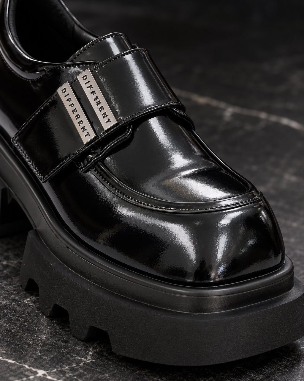 Gros plan sur la bride et les plaques argentées DIFFERENT de la chaussure plateforme femme noir brillant – DIFFERENT Paris