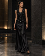 Femme portant le gilet noir à clous argentés et diamants DIFFERENT avec jupe longue en satin noir, dans un hall en marbre – DIFFERENT Paris