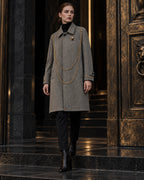 Femme portant le manteau long gris à chaînes dorées DIFFERENT fermé avec bottines noires, devant une porte en bronze – DIFFERENT Paris