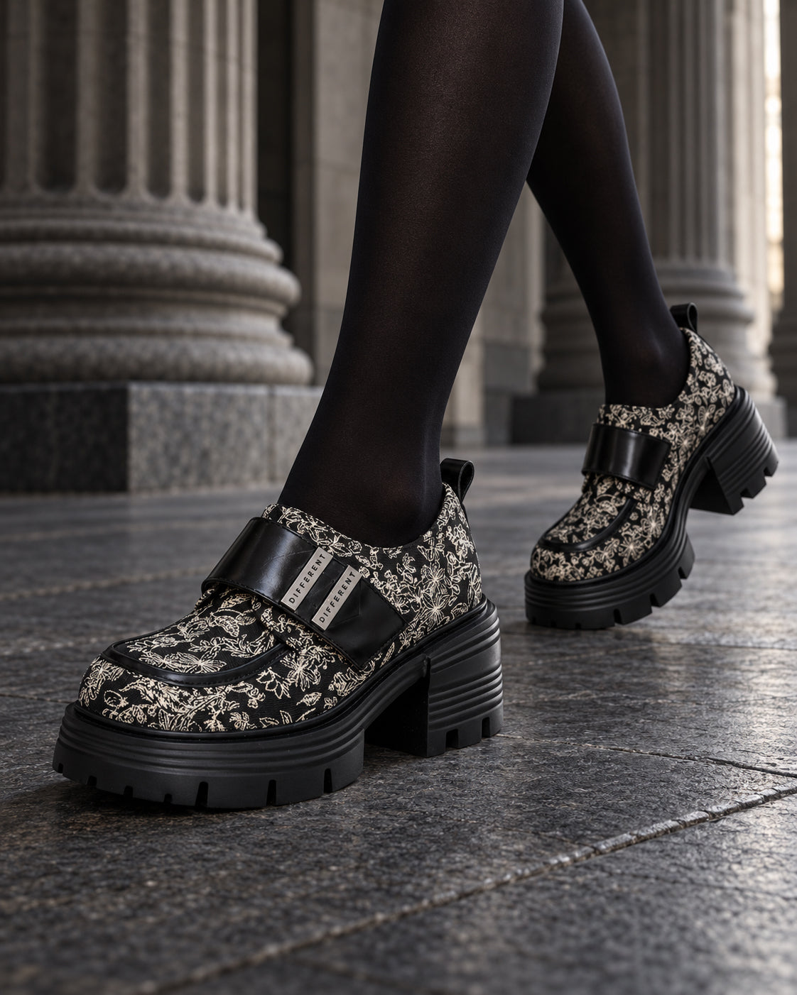 Chaussures à plateforme motif baroque DIFFERENT portées avec collants noirs, en marche devant des colonnes – DIFFERENT Paris