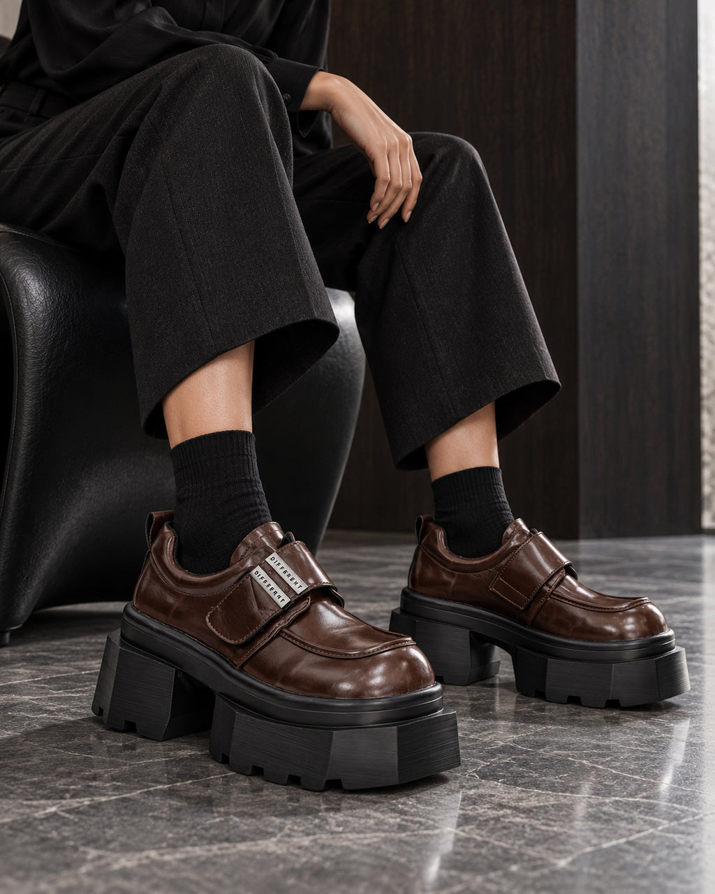Chaussures à plateforme marron brillant DIFFERENT portées avec pantalon large noir et chaussettes noires, assise – DIFFERENT Paris