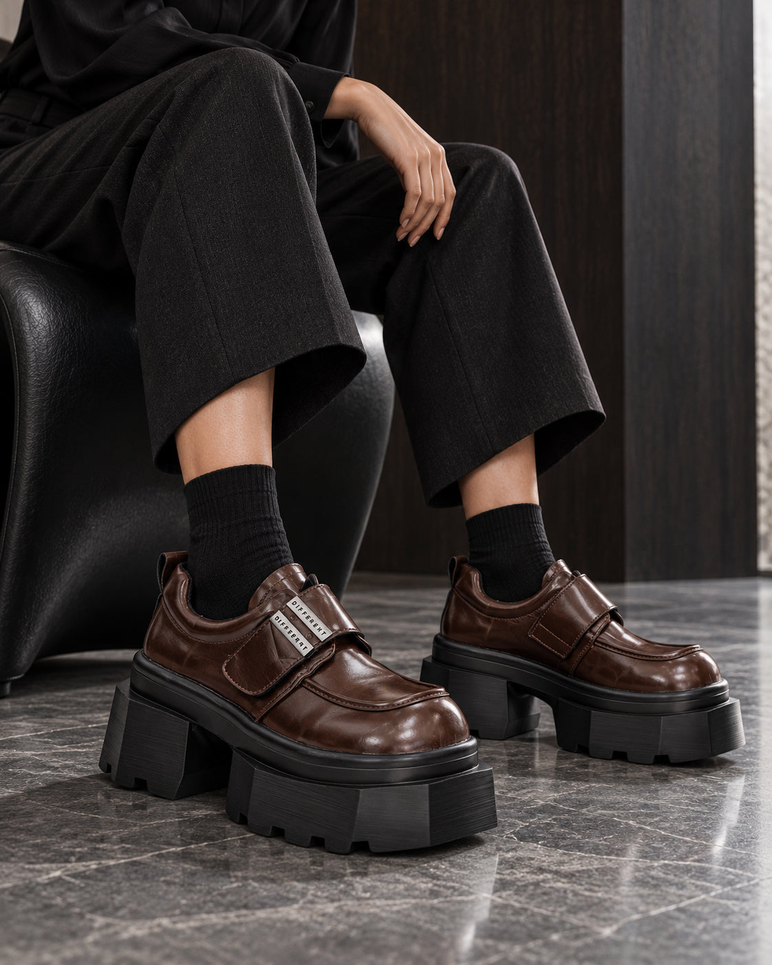 Chaussures à plateforme marron brillant DIFFERENT portées avec pantalon large noir et chaussettes noires, assise – DIFFERENT Paris
