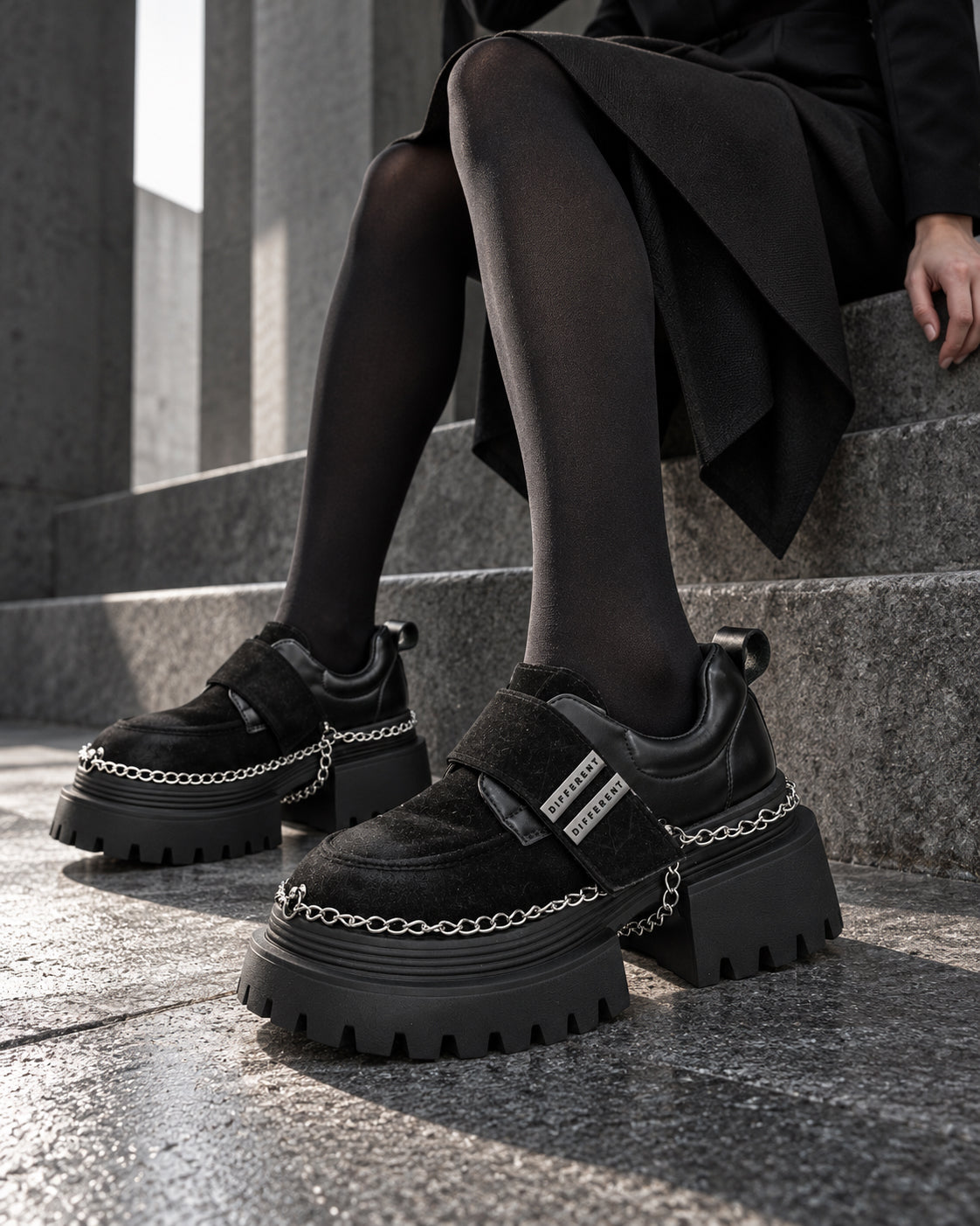 Chaussures à plateforme et chaînes DIFFERENT portées avec collants noirs, assise sur des marches en pierre – DIFFERENT Paris