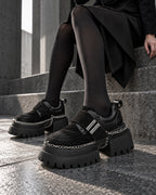 Chaussures à plateforme et chaînes DIFFERENT portées avec collants noirs, assise sur des marches en pierre – DIFFERENT Paris