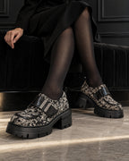 Chaussures à plateforme motif baroque DIFFERENT portées avec robe noire et collants noirs, jambes croisées – DIFFERENT Paris