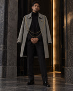 Homme portant le manteau long gris à chaînes dorées DIFFERENT ouvert sur un costume noir, dans un hall en marbre – DIFFERENT Paris