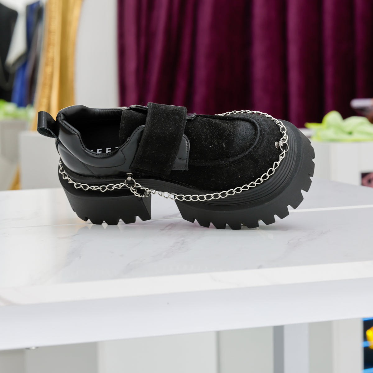 Chaussure noire vue de dessus et de côté, montrant le bout arrondi, la bride et la chaîne argentée.