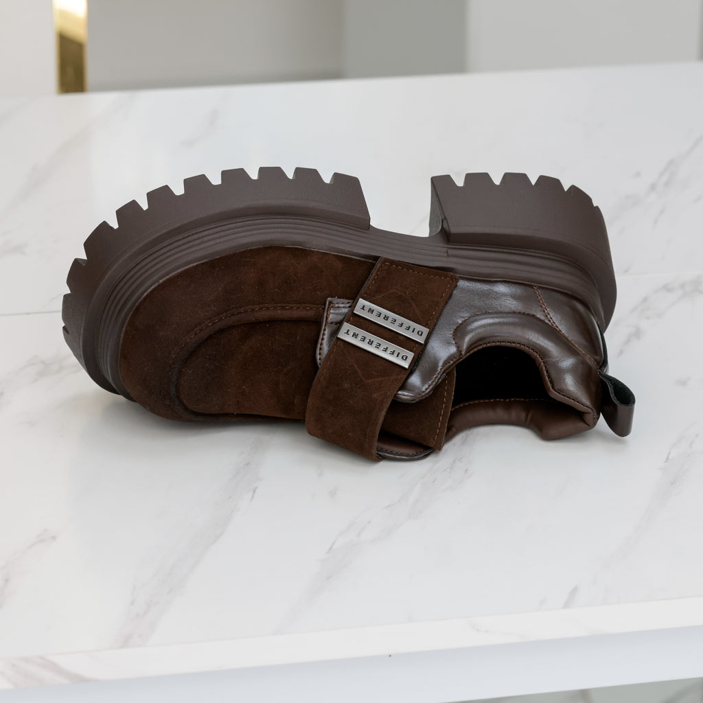 Chaussure marron chocolat posée sur le côté, montrant la large bride, les plaques argentées et la plateforme crantée.