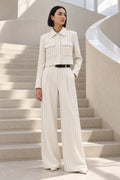 Veste courte à col chemise et pantalon tailleur blanc à fines rayures, devant un escalier