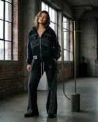Black HN jogging set worn by a woman in a brick workshop, rhinestone Hype Or Nothing sweatshirt and flared trousers – DIFFERENT Paris