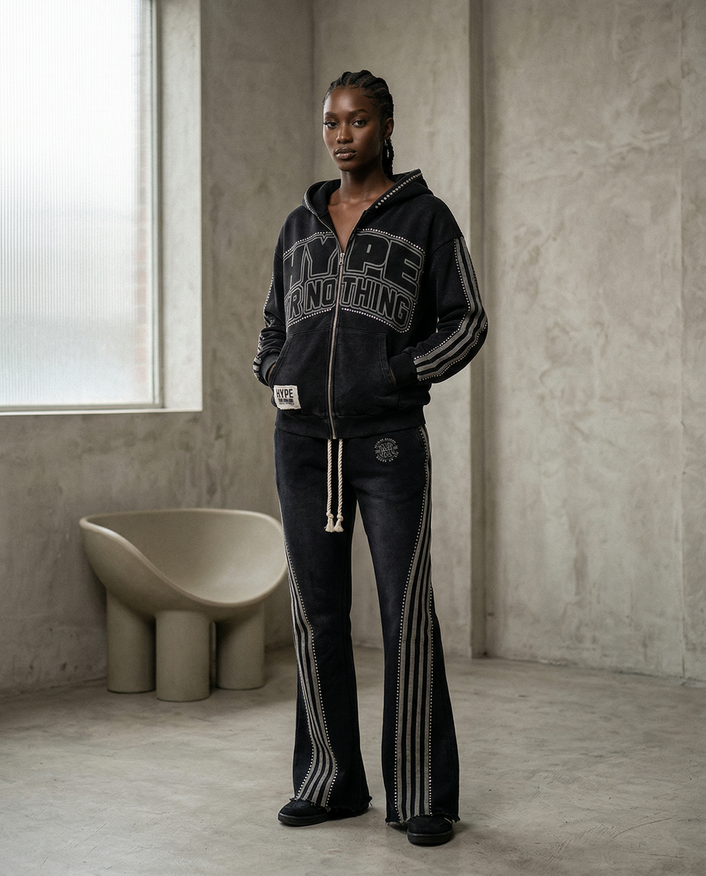 Black HN jogging set worn by a woman in a concrete loft, Hype Or Nothing zip-up hoodie and rhinestone striped trousers – DIFFERENT Paris