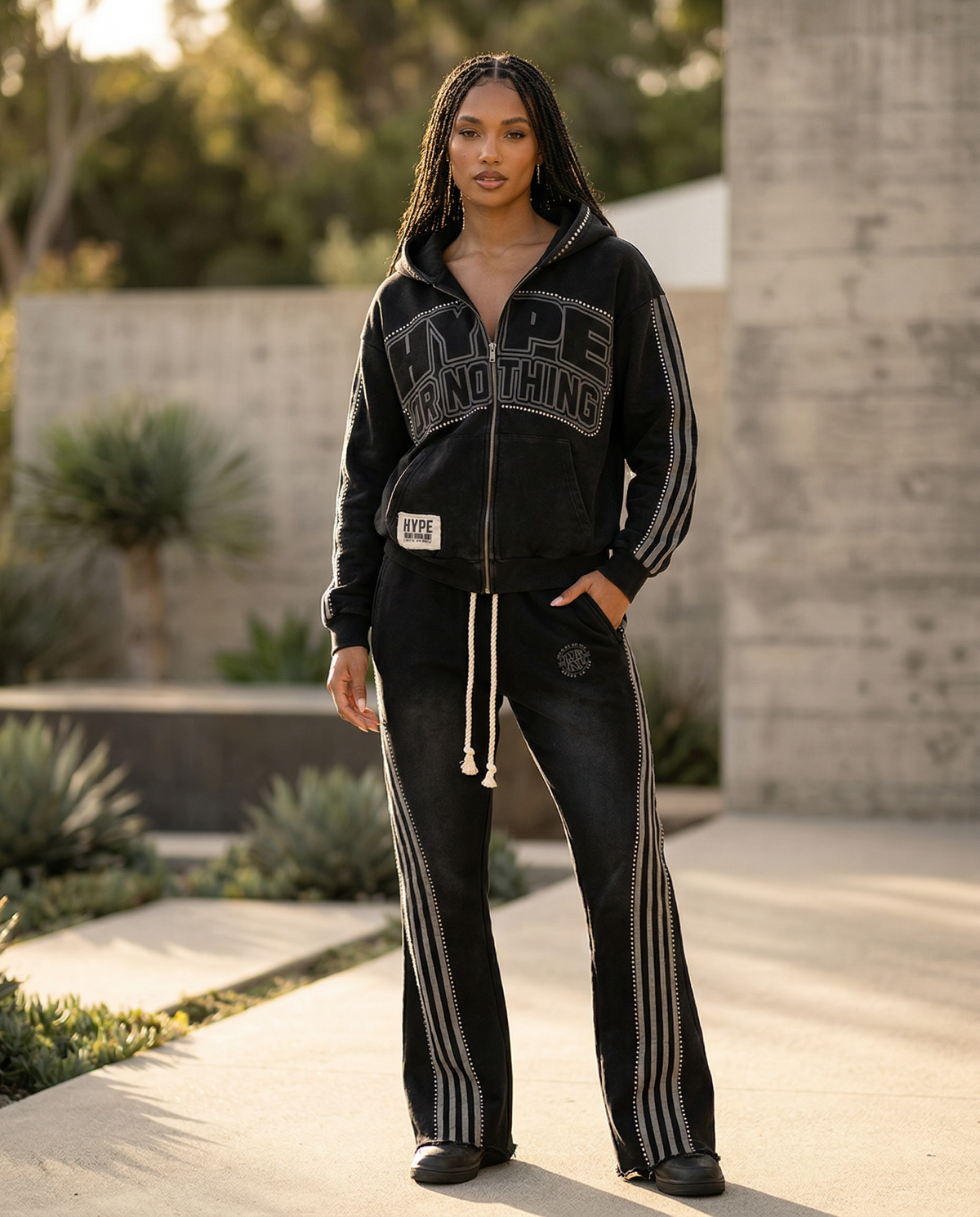Black HN jogging set worn by a woman outdoors in the sun, Hype Or Nothing hoodie and flared striped trousers – DIFFERENT Paris