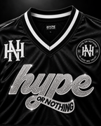Détail du col V blanc, monogramme HN et script hype or nothing en strass – DIFFERENT Paris